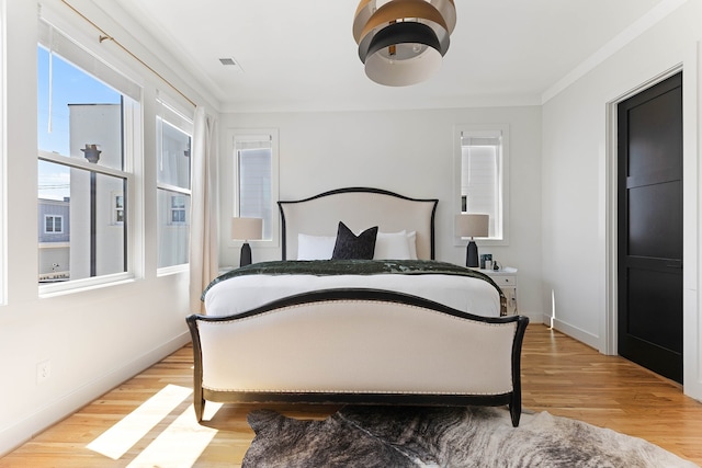 bedroom with multiple windows, light hardwood / wood-style floors, and ornamental molding