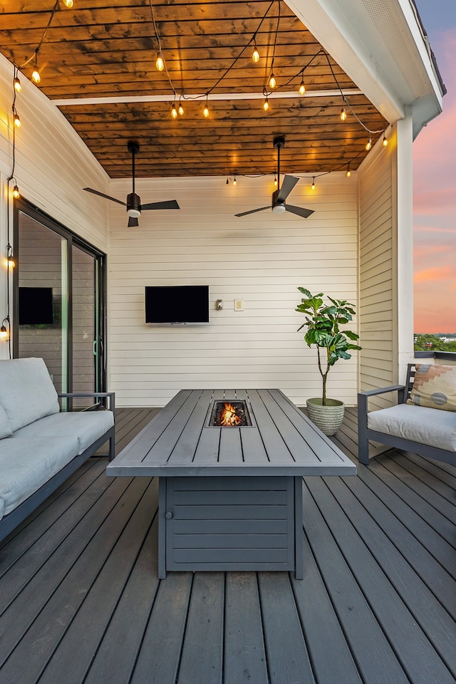 deck at dusk featuring ceiling fan and an outdoor living space with a fire pit