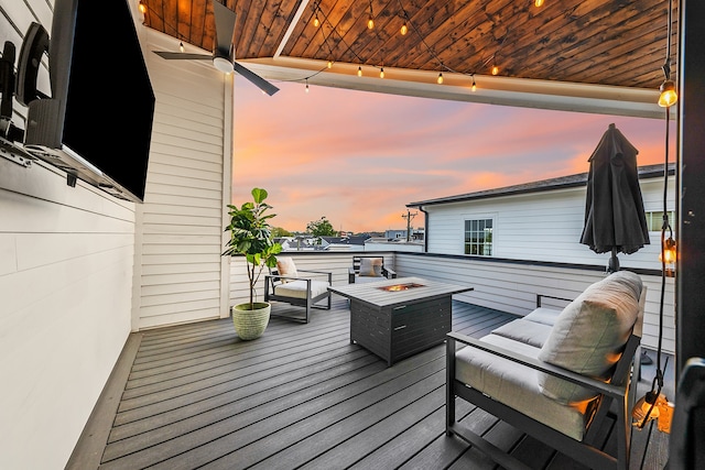 deck at dusk with ceiling fan and an outdoor living space with a fire pit