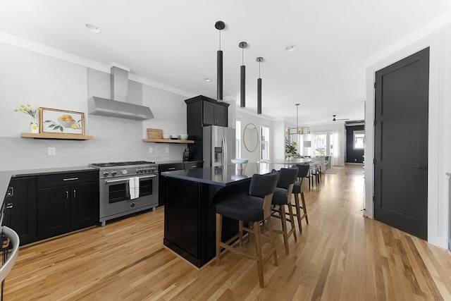 kitchen featuring a center island, wall chimney range hood, a kitchen bar, appliances with stainless steel finishes, and light wood-type flooring