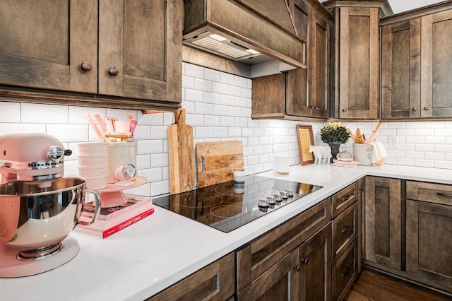 kitchen with dark brown cabinetry, dark hardwood / wood-style floors, black electric cooktop, decorative backsplash, and custom exhaust hood