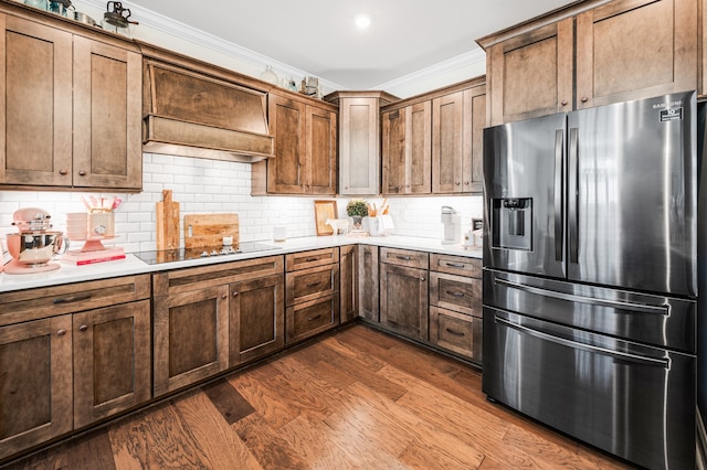 kitchen with stainless steel refrigerator with ice dispenser, backsplash, black electric cooktop, crown molding, and wood-type flooring