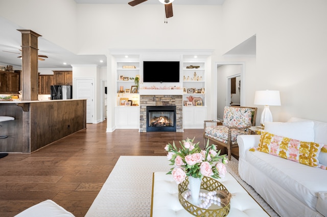 living room featuring ceiling fan, a high ceiling, a stone fireplace, built in features, and dark hardwood / wood-style flooring