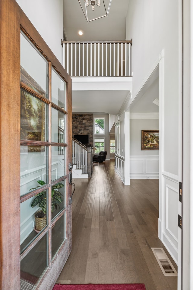 foyer entrance featuring a towering ceiling, dark wood-type flooring, a notable chandelier, and ornamental molding