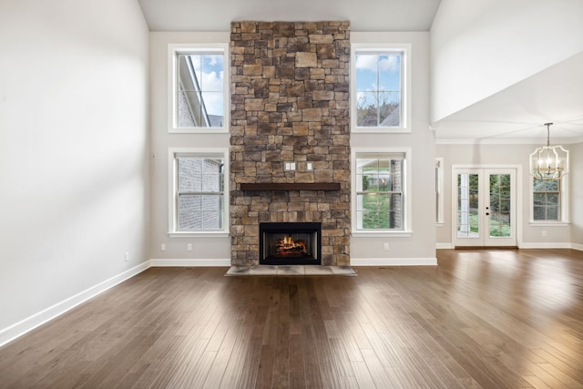 unfurnished living room featuring a stone fireplace, dark hardwood / wood-style flooring, high vaulted ceiling, and a notable chandelier