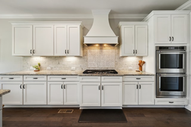 kitchen with premium range hood, dark wood-type flooring, appliances with stainless steel finishes, light stone counters, and white cabinetry