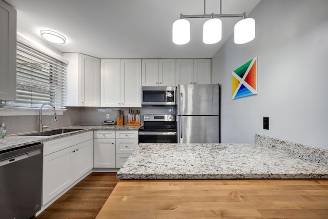 kitchen with pendant lighting, backsplash, white cabinets, sink, and stainless steel appliances