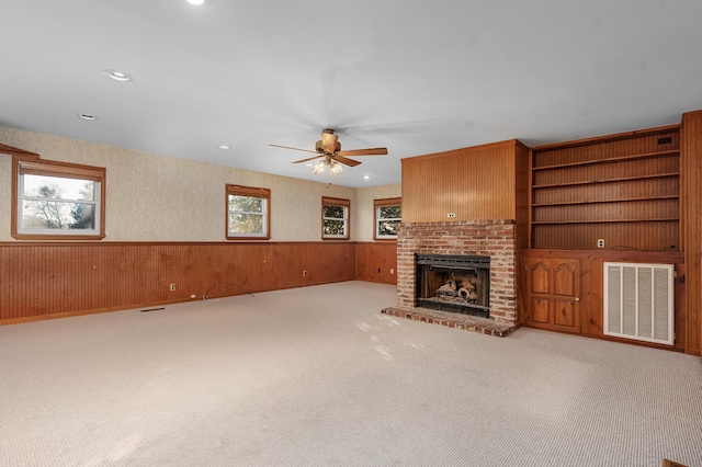 unfurnished living room featuring wooden walls, ceiling fan, light colored carpet, and a brick fireplace