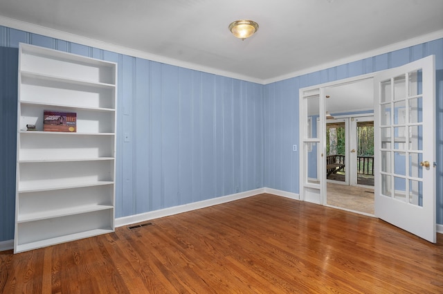 spare room with hardwood / wood-style flooring, built in shelves, ornamental molding, and french doors