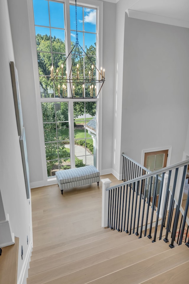 stairway with hardwood / wood-style floors, ornamental molding, and an inviting chandelier