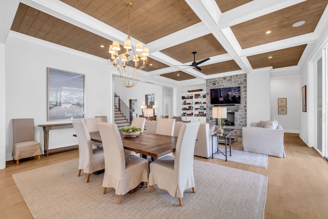 dining space with ceiling fan with notable chandelier, beam ceiling, a fireplace, and light hardwood / wood-style flooring