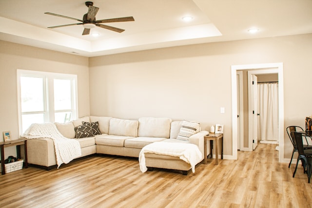 living room with a raised ceiling, light hardwood / wood-style flooring, and ceiling fan