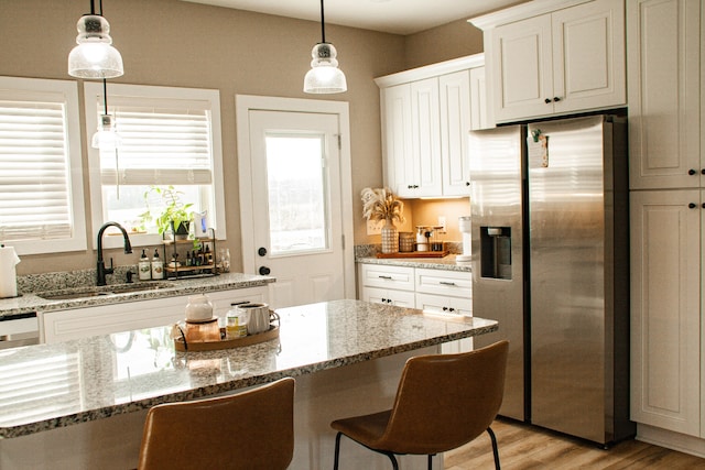 kitchen featuring white cabinets, sink, hanging light fixtures, stainless steel fridge, and light hardwood / wood-style floors