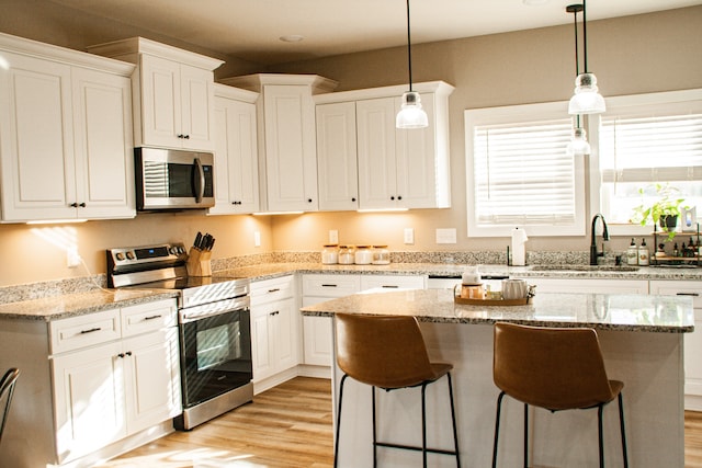 kitchen with sink, light wood-type flooring, a kitchen island, white cabinetry, and stainless steel appliances