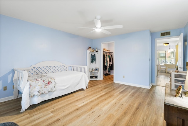 bedroom with a walk in closet, ceiling fan, a closet, and light hardwood / wood-style floors