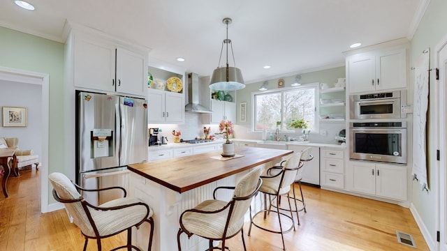 kitchen with white cabinetry, a center island, wall chimney exhaust hood, stainless steel appliances, and decorative light fixtures