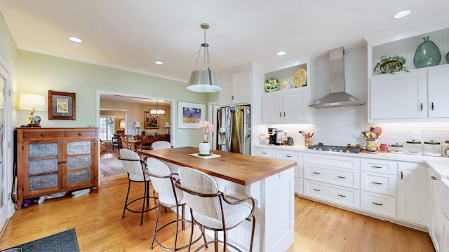 kitchen with a center island, wall chimney exhaust hood, appliances with stainless steel finishes, decorative light fixtures, and white cabinetry