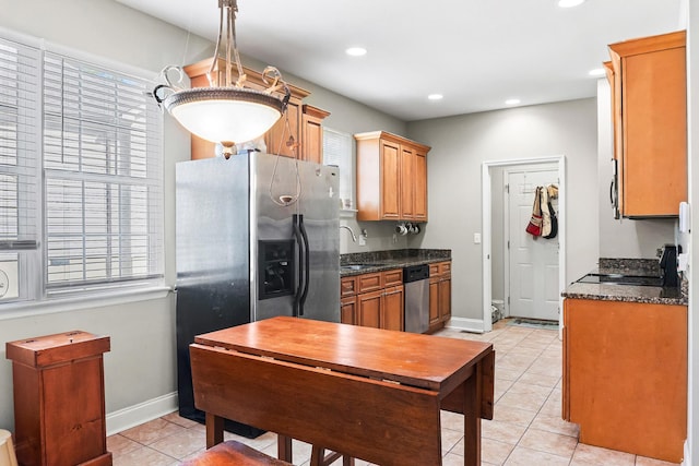 kitchen featuring stainless steel appliances, sink, light tile patterned floors, dark stone countertops, and hanging light fixtures