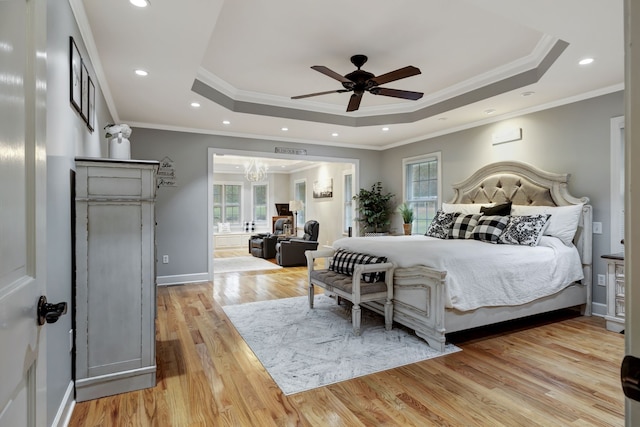 bedroom featuring a raised ceiling, light hardwood / wood-style flooring, ceiling fan with notable chandelier, and ornamental molding