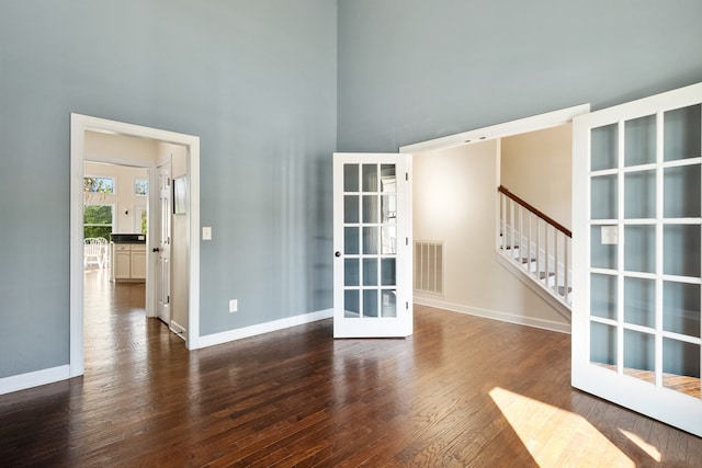 unfurnished room with dark hardwood / wood-style flooring, a towering ceiling, and french doors