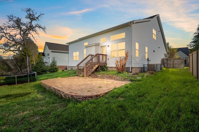 back house at dusk with a yard, a patio, a trampoline, and central AC