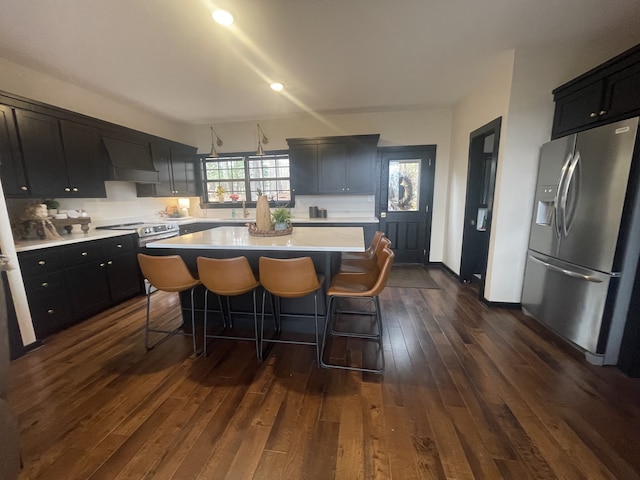 kitchen featuring dark hardwood / wood-style flooring, premium range hood, a kitchen bar, a kitchen island, and appliances with stainless steel finishes