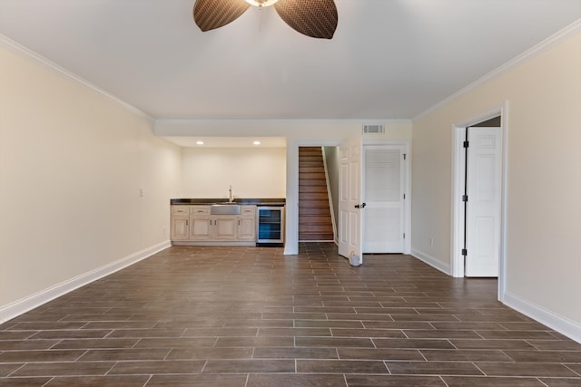 unfurnished living room with ceiling fan, ornamental molding, beverage cooler, and wet bar