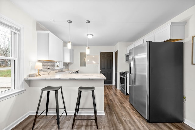 kitchen featuring kitchen peninsula, appliances with stainless steel finishes, white cabinetry, and hanging light fixtures