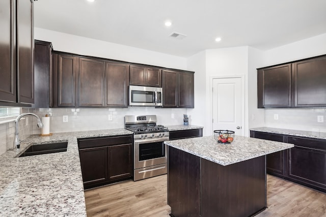 kitchen featuring appliances with stainless steel finishes, light wood-type flooring, light stone counters, and sink