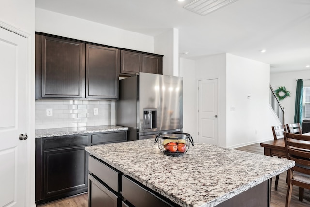 kitchen with stainless steel fridge with ice dispenser, a kitchen island, light hardwood / wood-style floors, and light stone counters