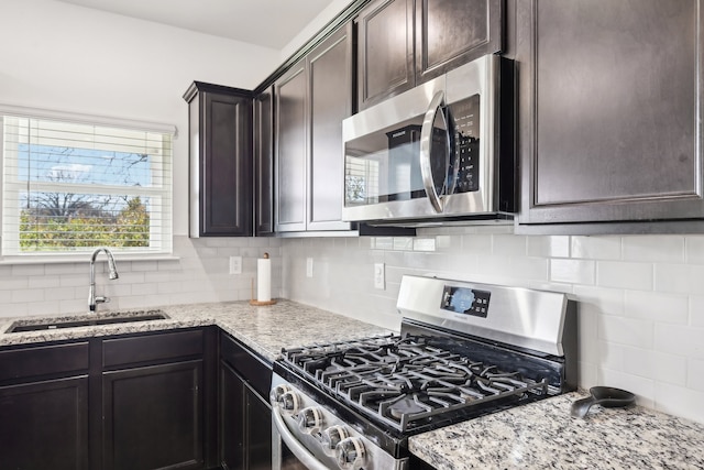 kitchen featuring sink, light stone countertops, appliances with stainless steel finishes, tasteful backsplash, and dark brown cabinetry