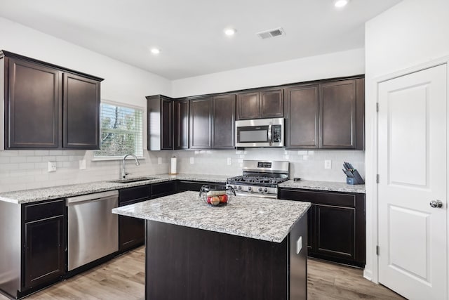 kitchen featuring sink, a center island, stainless steel appliances, light stone counters, and light wood-type flooring