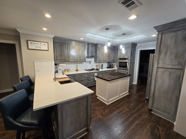 kitchen featuring sink, stainless steel appliances, wall chimney range hood, kitchen peninsula, and decorative light fixtures