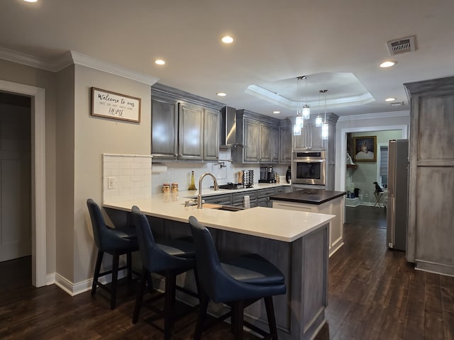 kitchen featuring dark wood-type flooring, hanging light fixtures, wall chimney exhaust hood, appliances with stainless steel finishes, and kitchen peninsula