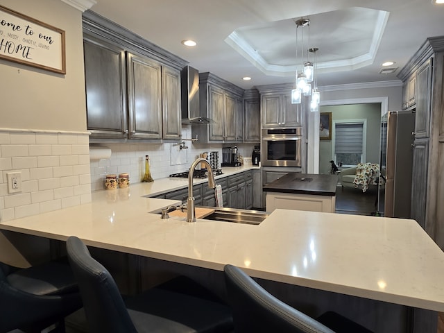 kitchen featuring kitchen peninsula, wall chimney exhaust hood, a raised ceiling, sink, and hanging light fixtures