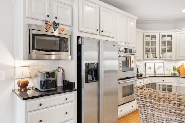 kitchen with appliances with stainless steel finishes, ornamental molding, white cabinets, and tasteful backsplash