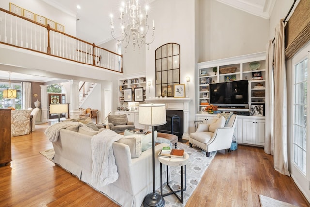 living room with a towering ceiling, wood-type flooring, built in shelves, a notable chandelier, and crown molding