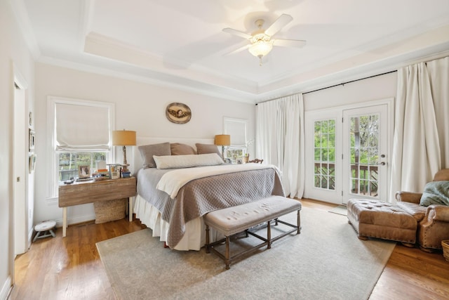 bedroom with ceiling fan, access to exterior, a tray ceiling, hardwood / wood-style flooring, and ornamental molding