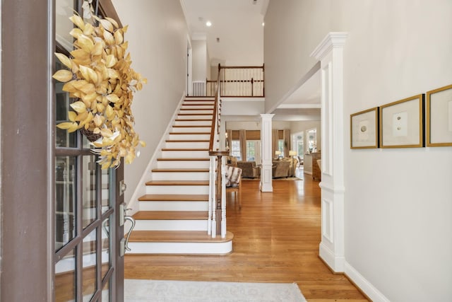 entryway with decorative columns, light hardwood / wood-style floors, a high ceiling, and crown molding