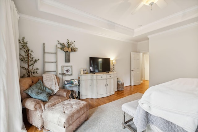 bedroom featuring ceiling fan, light wood-type flooring, ornamental molding, and a raised ceiling