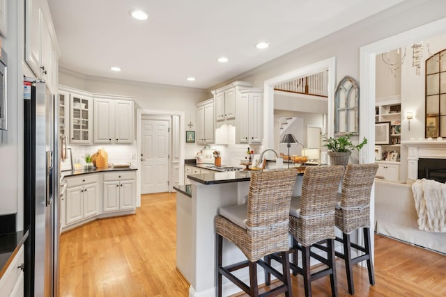 kitchen with stainless steel refrigerator with ice dispenser, white cabinetry, light hardwood / wood-style floors, a kitchen breakfast bar, and kitchen peninsula