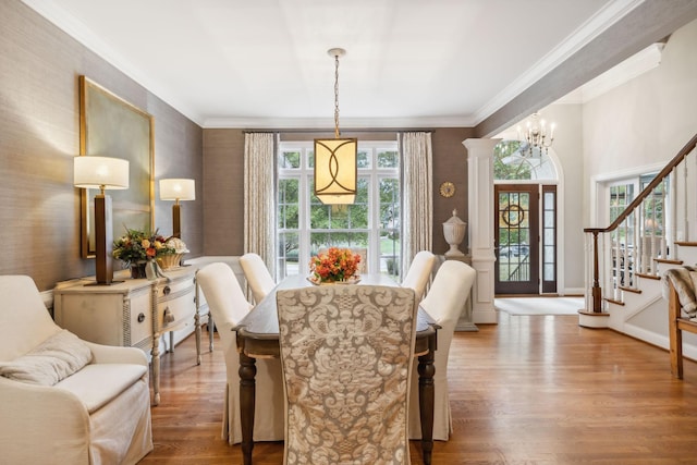 dining room featuring decorative columns, hardwood / wood-style floors, ornamental molding, and an inviting chandelier