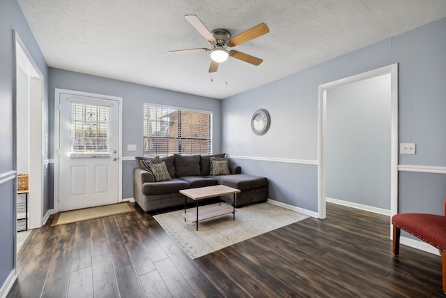 living room with a textured ceiling, ceiling fan, and dark wood-type flooring