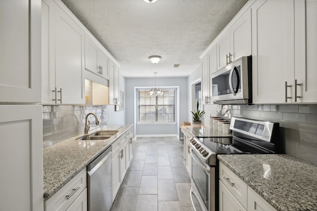 kitchen featuring sink, hanging light fixtures, backsplash, white cabinets, and appliances with stainless steel finishes