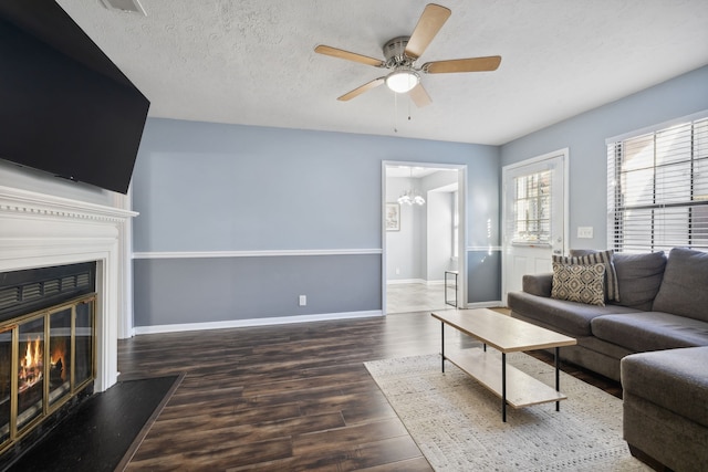 living room featuring ceiling fan with notable chandelier, a textured ceiling, and dark wood-type flooring