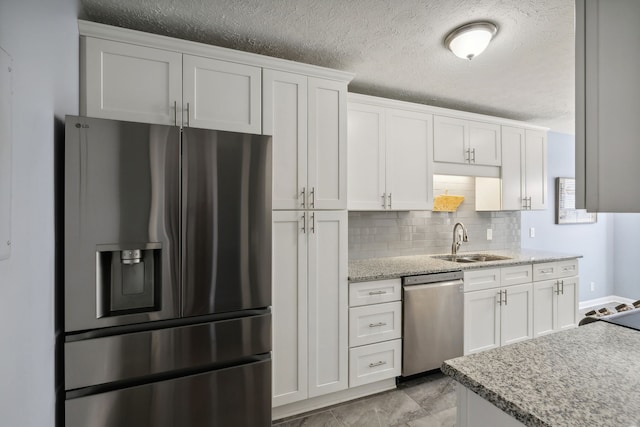 kitchen with white cabinetry, sink, light stone countertops, tasteful backsplash, and appliances with stainless steel finishes