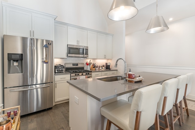 kitchen with white cabinetry, dark hardwood / wood-style floors, a kitchen bar, a kitchen island with sink, and appliances with stainless steel finishes