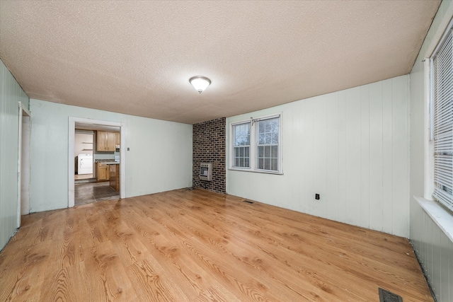 interior space with a textured ceiling, heating unit, wooden walls, light hardwood / wood-style flooring, and washer / dryer