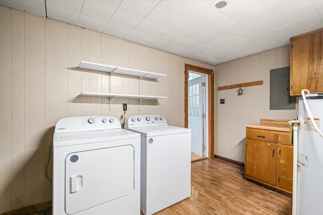 clothes washing area with light wood-type flooring, electric panel, washer and clothes dryer, and wooden walls