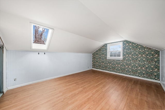 additional living space with lofted ceiling with skylight and hardwood / wood-style floors